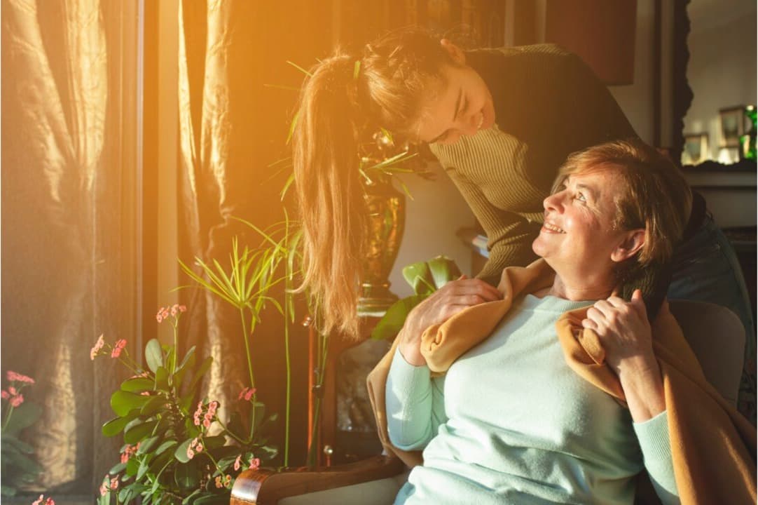 A carer sitting comfortably beside an elderly person in a living room